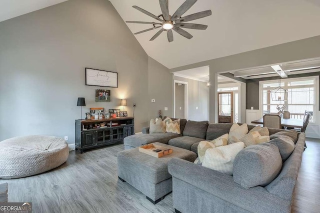 living area with ceiling fan with notable chandelier, high vaulted ceiling, and wood finished floors