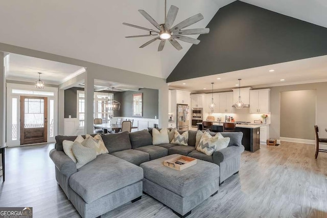 living area featuring ceiling fan with notable chandelier, high vaulted ceiling, light wood-style floors, and crown molding