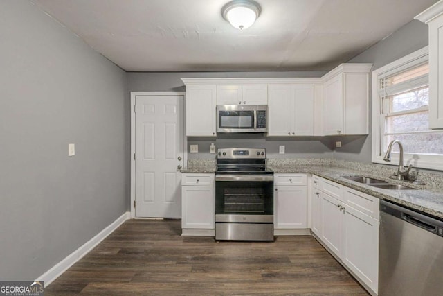 kitchen with dark wood-type flooring, a sink, white cabinetry, appliances with stainless steel finishes, and light stone countertops