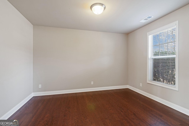 unfurnished room with baseboards, visible vents, and dark wood finished floors