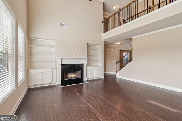 unfurnished living room featuring visible vents, stairway, dark wood-type flooring, a lit fireplace, and baseboards