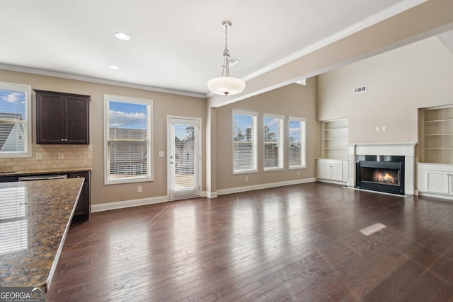 unfurnished living room with a warm lit fireplace, visible vents, baseboards, and dark wood-style flooring