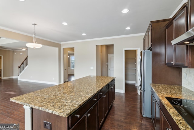 kitchen featuring black electric cooktop, a kitchen island, wall chimney range hood, light stone countertops, and pendant lighting