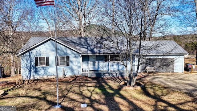 view of front of property with an attached garage, dirt driveway, a front lawn, and metal roof