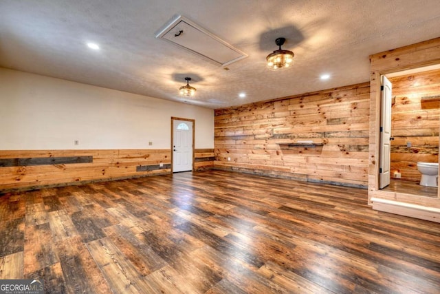 spare room featuring attic access, dark wood-style floors, a wainscoted wall, wood walls, and recessed lighting