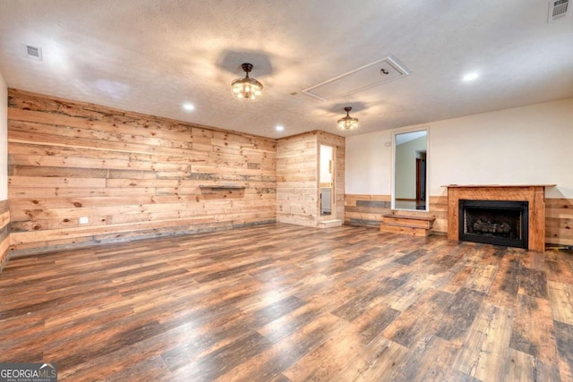 unfurnished living room with visible vents, dark wood finished floors, attic access, and wooden walls