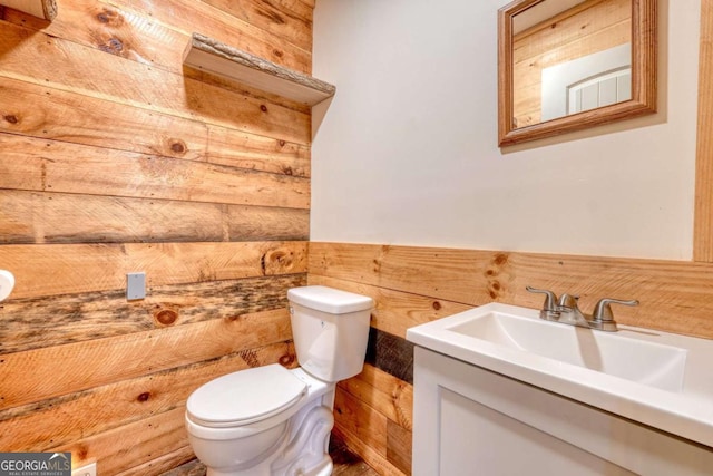 bathroom featuring wood walls, wainscoting, vanity, and toilet