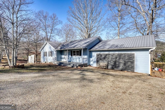 ranch-style house featuring a porch, metal roof, driveway, and an attached garage