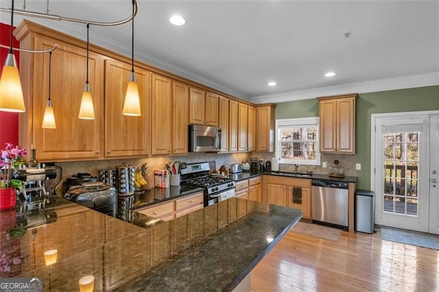 kitchen with appliances with stainless steel finishes, dark stone countertops, a peninsula, crown molding, and pendant lighting