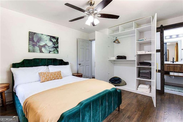 bedroom with a barn door, ceiling fan, and dark wood-type flooring