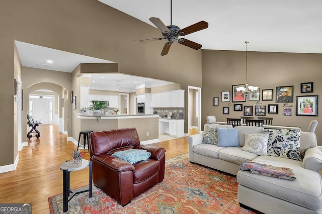 living room with arched walkways, light wood-style floors, high vaulted ceiling, baseboards, and ceiling fan with notable chandelier