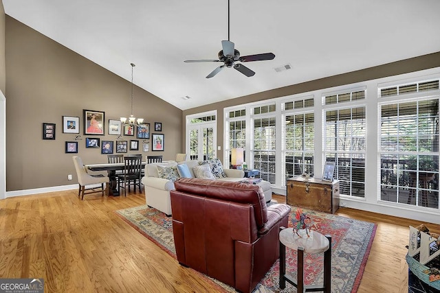 living room with high vaulted ceiling, light wood-style flooring, ceiling fan with notable chandelier, visible vents, and baseboards