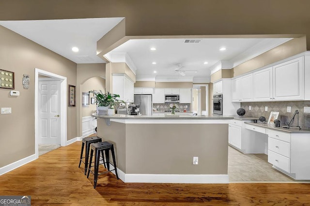 kitchen featuring arched walkways, a breakfast bar area, stainless steel appliances, visible vents, and white cabinets