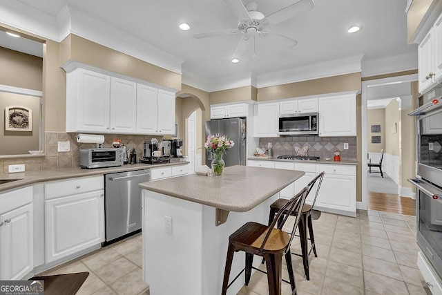 kitchen with arched walkways, a center island, stainless steel appliances, ornamental molding, and a kitchen breakfast bar