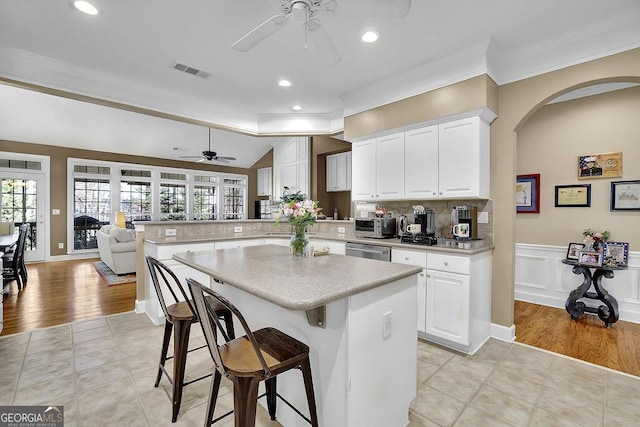 kitchen with light countertops, visible vents, stainless steel dishwasher, a peninsula, and a kitchen breakfast bar