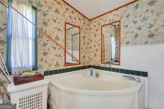 bathroom with a bath, wallpapered walls, ornamental molding, and a textured ceiling