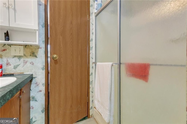 full bathroom featuring an enclosed shower, vanity, and wallpapered walls