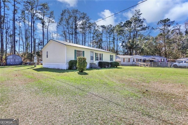 manufactured / mobile home with fence, a storage unit, a front lawn, and an outbuilding