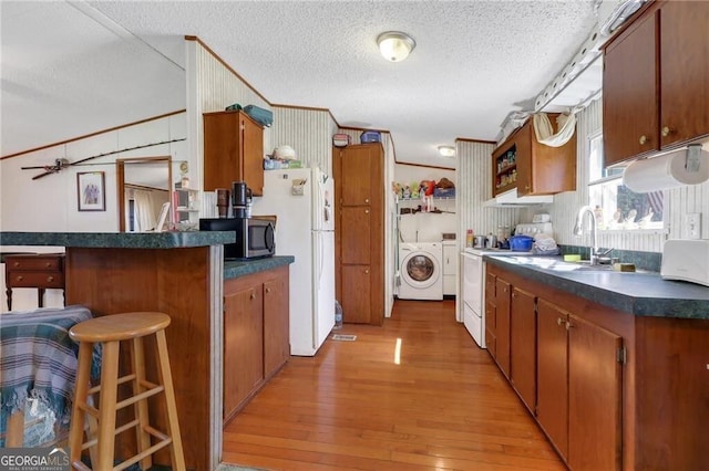 kitchen featuring dark countertops, white appliances, brown cabinetry, and washing machine and clothes dryer