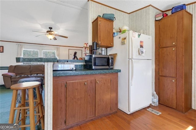 kitchen featuring stainless steel microwave, ornamental molding, freestanding refrigerator, brown cabinetry, and dark countertops