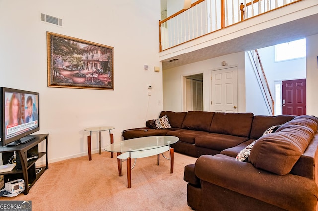 living area featuring carpet floors, visible vents, a towering ceiling, and baseboards