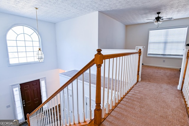 hallway featuring light carpet, a textured ceiling, and an upstairs landing