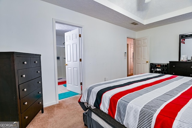 bedroom featuring visible vents, light colored carpet, a textured ceiling, and ensuite bath