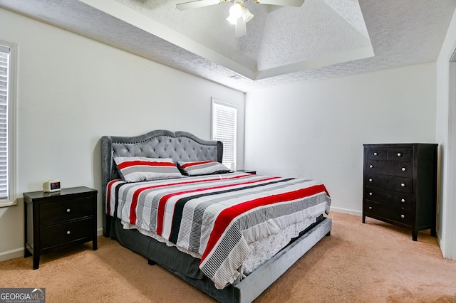 bedroom with a raised ceiling, light carpet, a textured ceiling, and baseboards