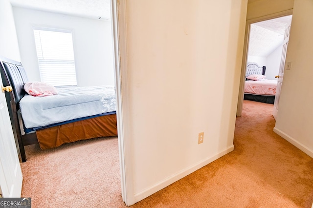 hall featuring baseboards, vaulted ceiling, a textured ceiling, and light colored carpet