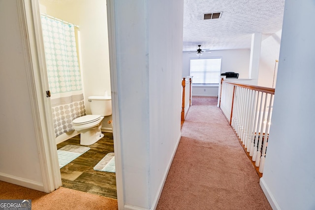 hall with a textured ceiling, carpet floors, wood finished floors, visible vents, and baseboards