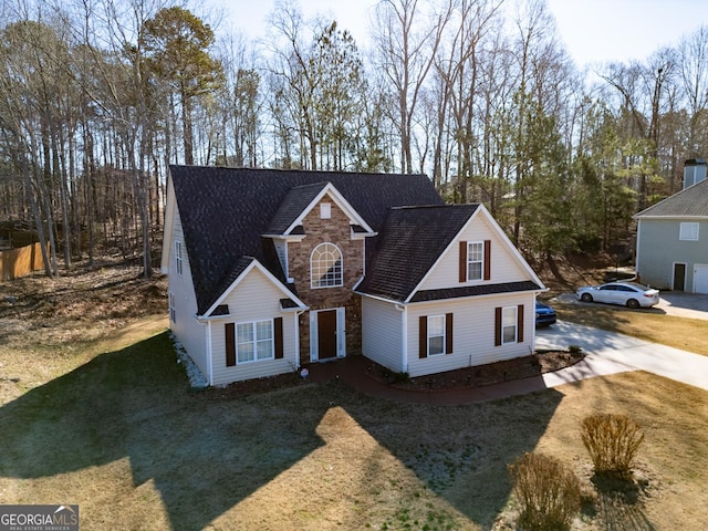 traditional-style house featuring stone siding, a front yard, and concrete driveway