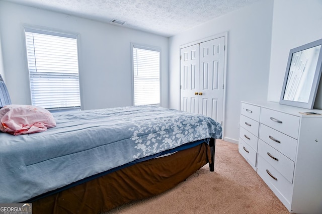 bedroom with a textured ceiling, a closet, visible vents, and light colored carpet