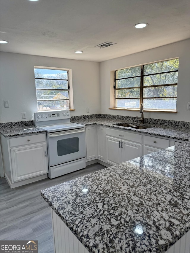 kitchen featuring a sink, visible vents, white cabinetry, dark stone counters, and white range with electric cooktop