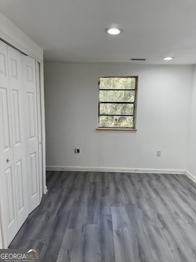 unfurnished bedroom with a closet, dark wood finished floors, visible vents, and baseboards