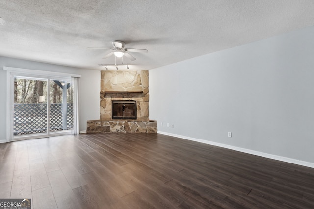 unfurnished living room with baseboards, a ceiling fan, dark wood-style flooring, a textured ceiling, and a stone fireplace