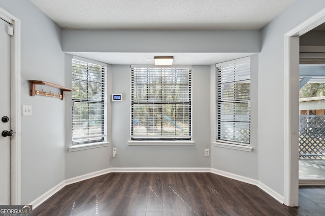 unfurnished dining area with baseboards, dark wood finished floors, and a textured ceiling