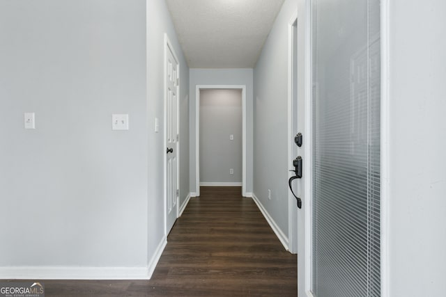 corridor featuring a textured ceiling, dark wood-type flooring, and baseboards