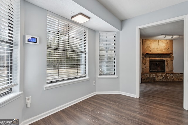 unfurnished dining area featuring dark wood-style floors, a fireplace, baseboards, and track lighting