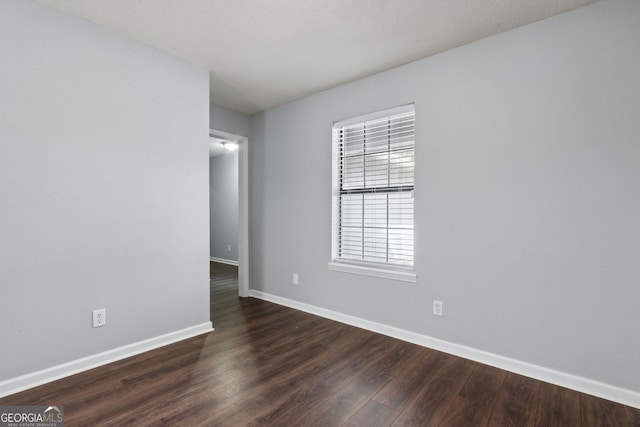 unfurnished room featuring baseboards and dark wood-style flooring