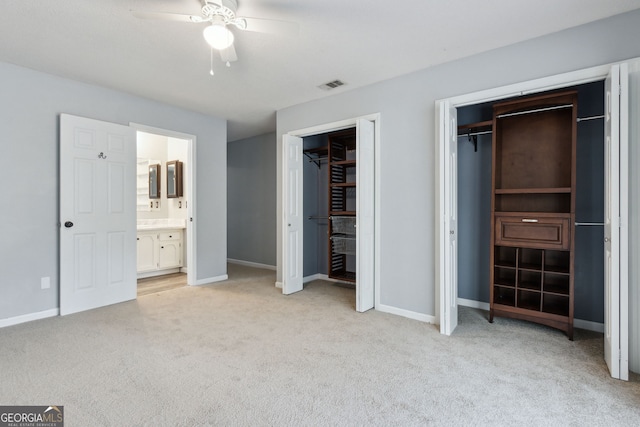 unfurnished bedroom with visible vents, light carpet, baseboards, and two closets