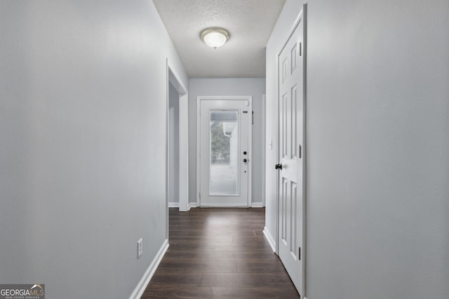 corridor with a textured ceiling, dark wood-type flooring, and baseboards