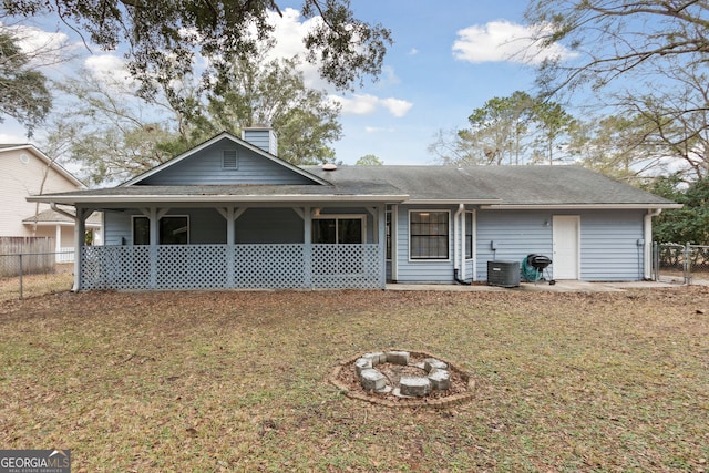 rear view of property featuring a fire pit, a lawn, a chimney, and fence