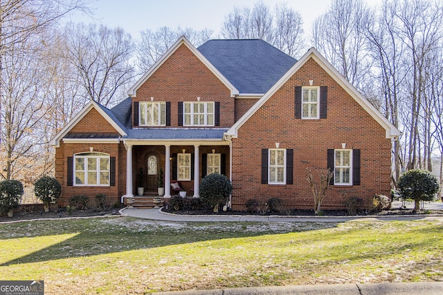 traditional home featuring covered porch, brick siding, a front lawn, and roof with shingles