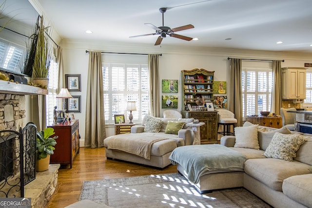 living area with light wood-style flooring, a fireplace, ornamental molding, and recessed lighting