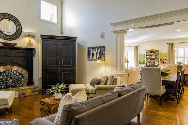 living room with dark wood-style floors, decorative columns, and a fireplace with raised hearth