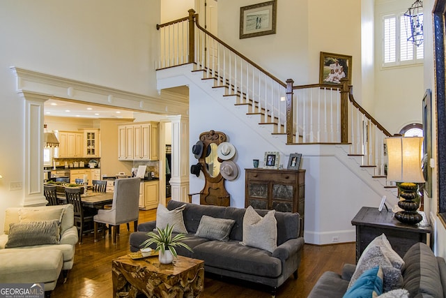 living area with a towering ceiling, dark wood-style flooring, stairway, and ornate columns