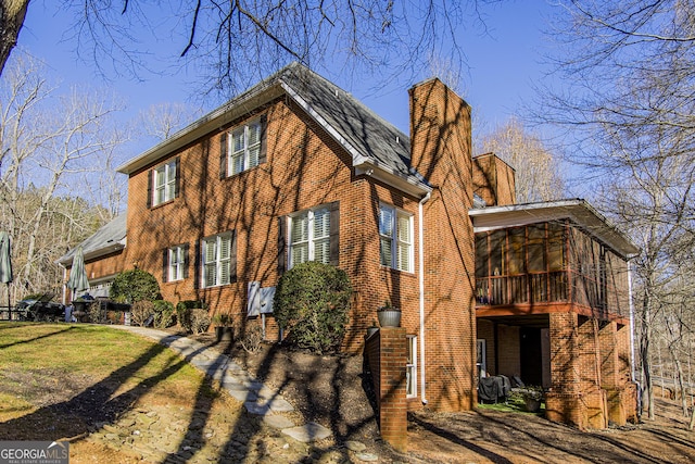 view of property exterior featuring a sunroom, brick siding, and a chimney