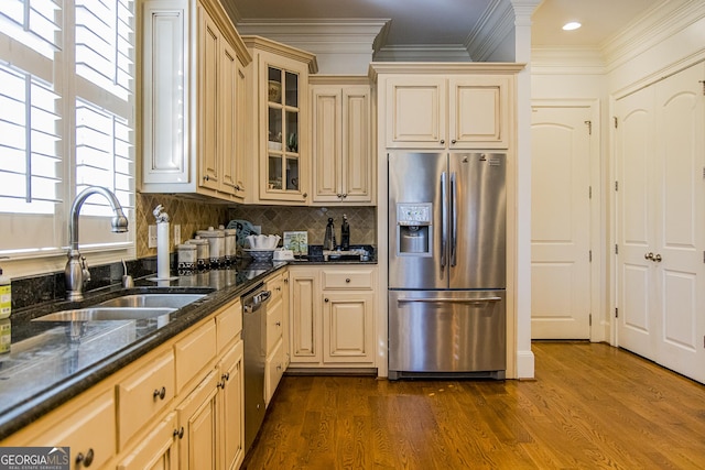 kitchen featuring a sink, appliances with stainless steel finishes, dark stone counters, glass insert cabinets, and crown molding