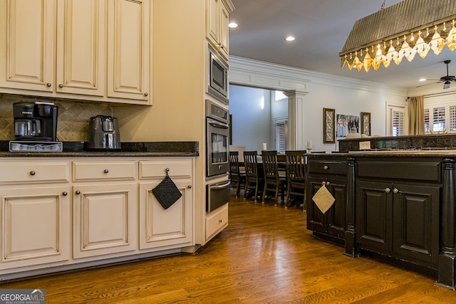 kitchen featuring dark wood finished floors, a warming drawer, stainless steel appliances, ornamental molding, and dark stone countertops