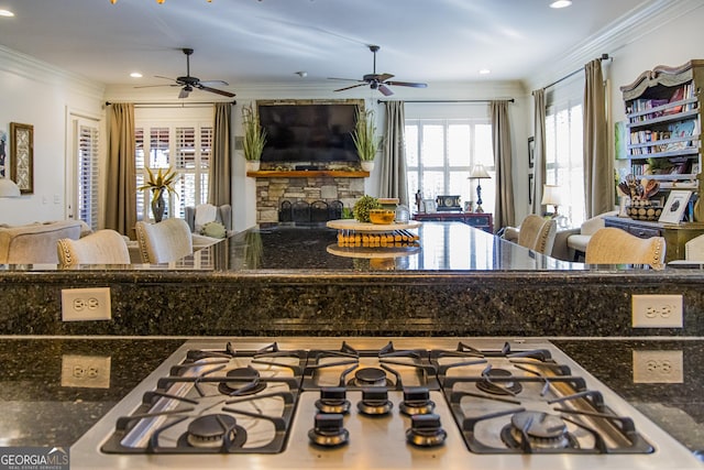 kitchen featuring a fireplace, gas stovetop, ornamental molding, open floor plan, and dark stone counters